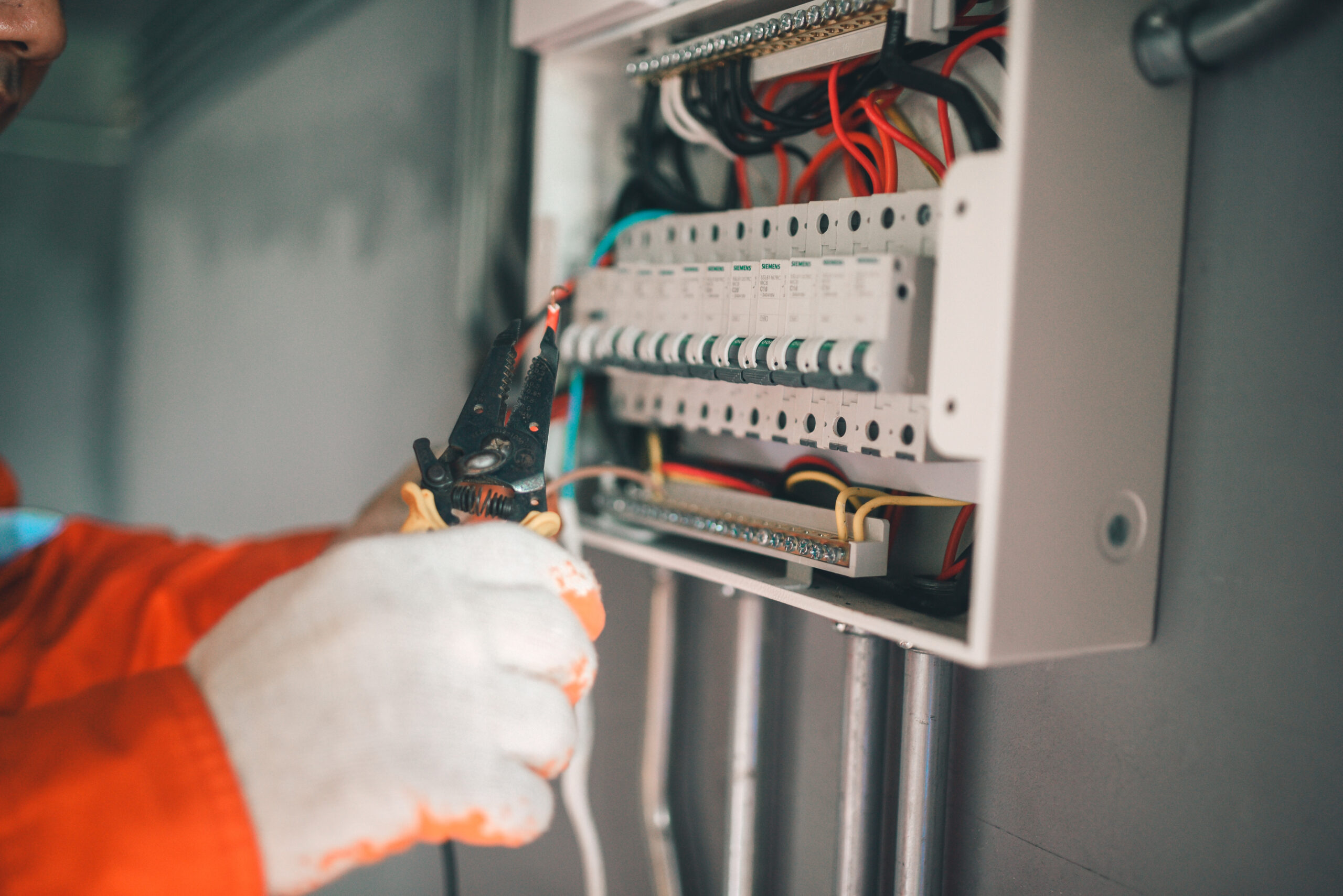 Side view of a handsome Asian electrician repairing an electrical box with pliers in the corridor.